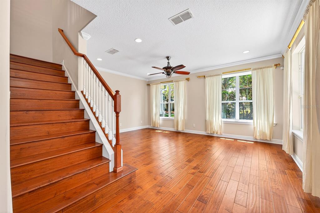A living room with hardwood floors, a wooden staircase, and large windows with white curtains — 7330 BRIGHTLAND STREET, WINDERMERE, FL