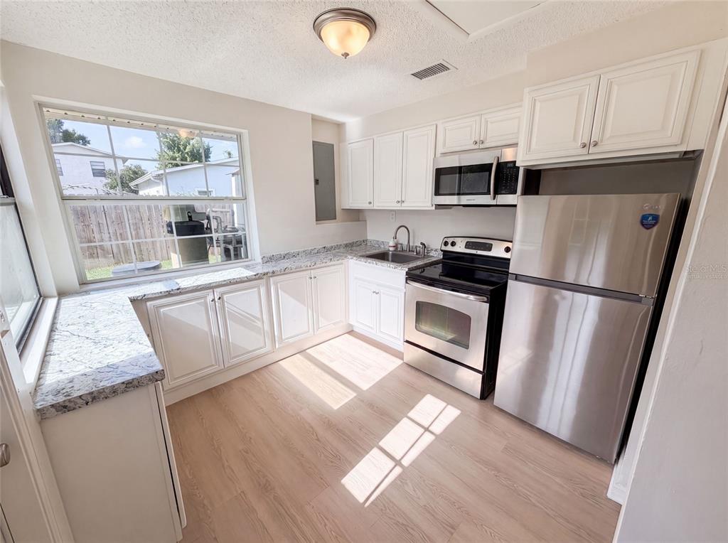 A kitchen with white cabinets, granite countertops, stainless steel appliances, and light wood-look flooring — 3665 MIAMI AVENUE, MELBOURNE, FL