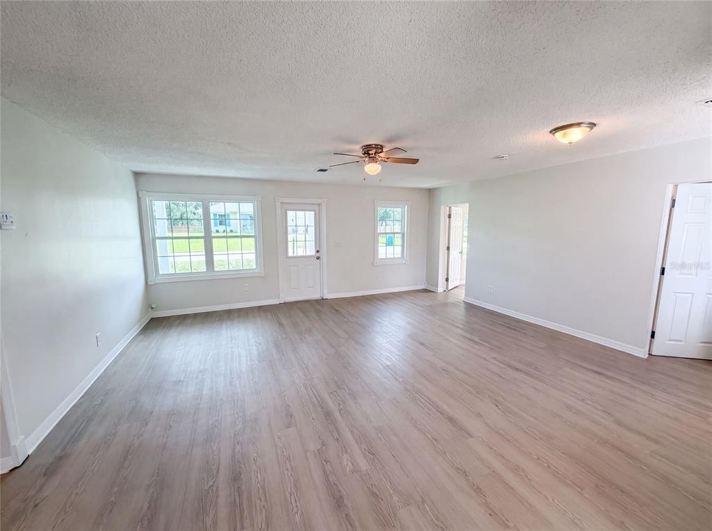 A living room with light wood-look flooring, a ceiling fan, and a white exterior door — 3665 MIAMI AVENUE, MELBOURNE, FL