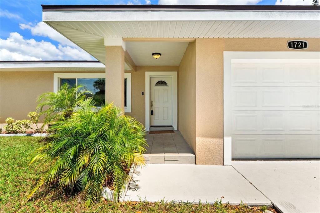 The exterior of a house features a white front door, a garage, and a palm tree — 1721 S JEFFERSON AVENUE, CLEARWATER, FL