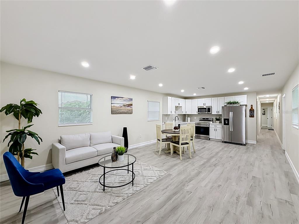 An open-concept living room and kitchen featuring light wood-look flooring and white cabinetry — 38910 MERRELL AVENUE, UMATILLA, FL