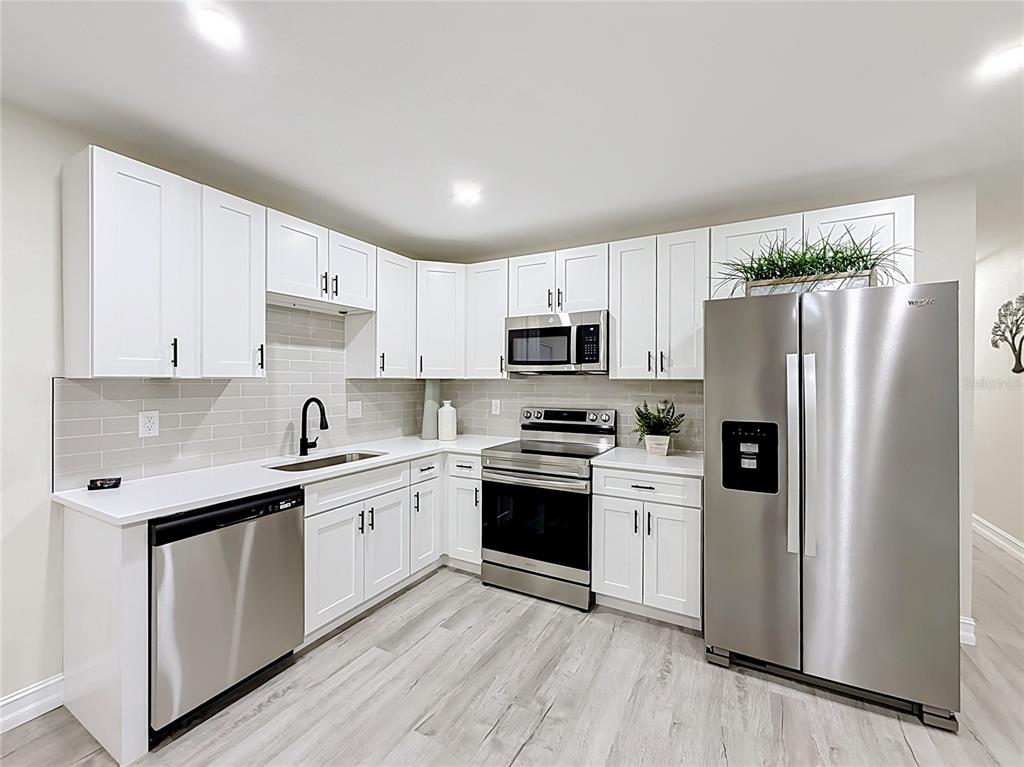A modern kitchen features white cabinets, stainless steel appliances, a subway tile backsplash, and light flooring — 38910 MERRELL AVENUE, UMATILLA, FL