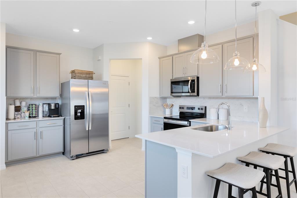 A modern kitchen features light gray cabinets, stainless steel appliances, and a white quartz island — 4357 JETTY LANE NE, PALM BAY, FL