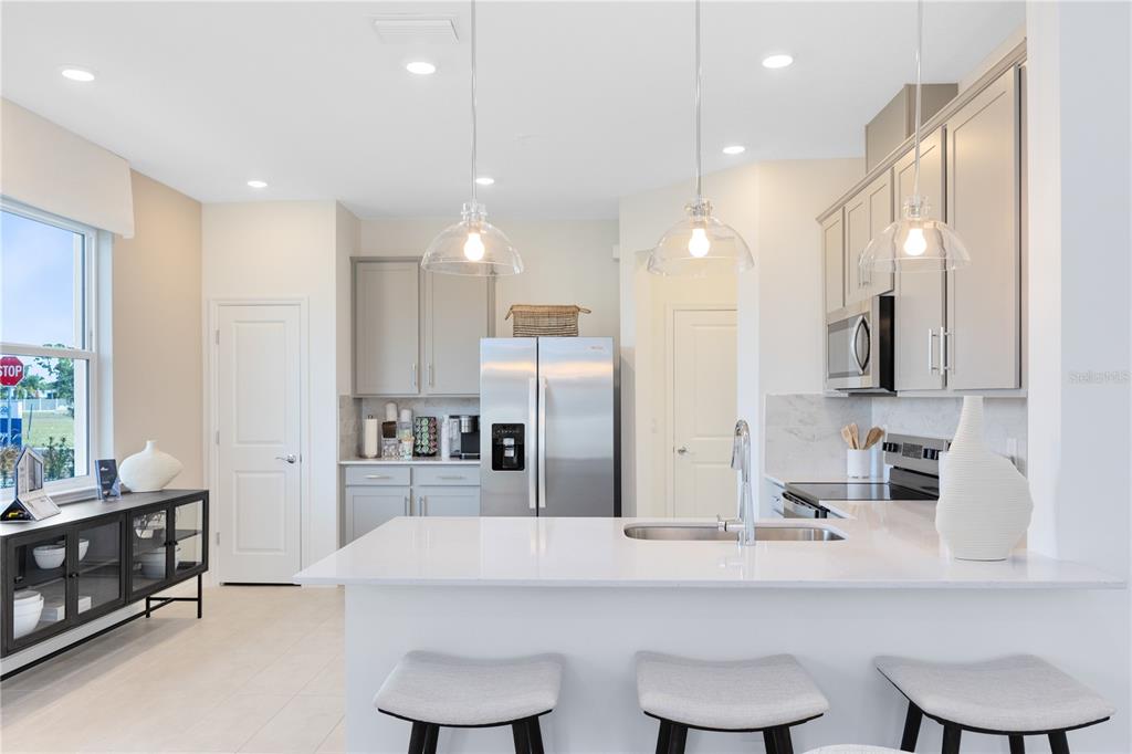 A modern kitchen features white countertops, gray cabinetry, stainless steel appliances, and three bar stools — 4357 JETTY LANE NE, PALM BAY, FL