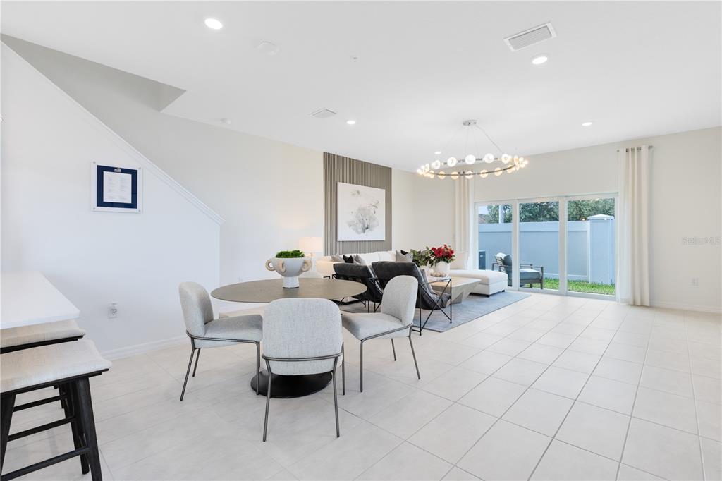 A bright open-concept living and dining area features tile flooring, a modern chandelier, and sliding doors — 4357 JETTY LANE NE, PALM BAY, FL