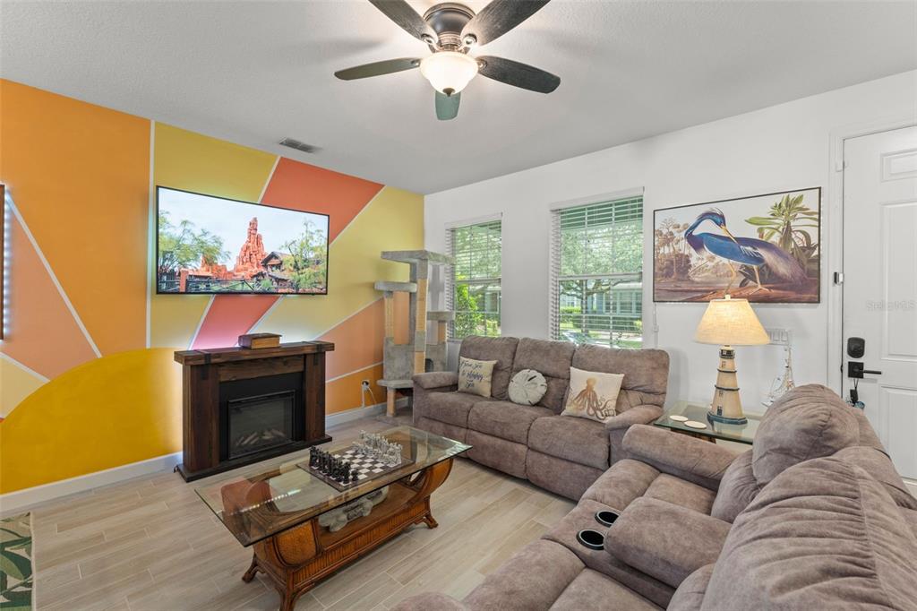 A living room features a sunburst-painted wall, a fireplace, a television, and brown sofas — 8481 LEELAND ARCHER BOULEVARD, ORLANDO, FL