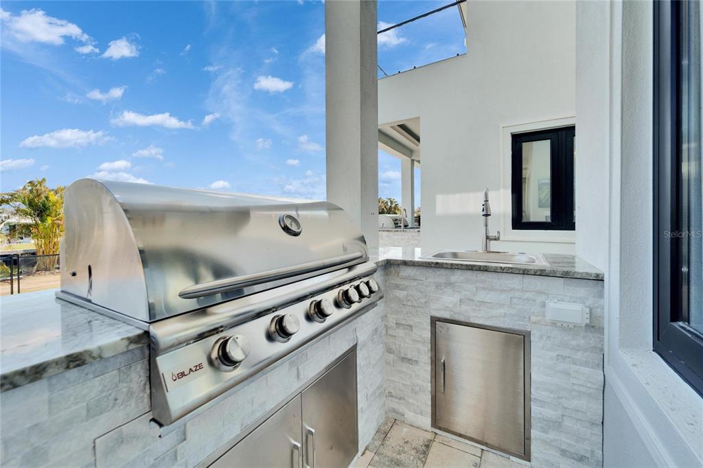 An outdoor kitchen features a stainless steel Blaze grill, a sink, and stone tile finishes — 6536 SIMONE SHORES CIRCLE, APOLLO BEACH, FL