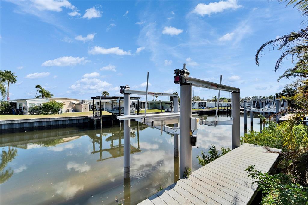 A boat lift stands over a canal next to a wooden dock under a blue sky — 6536 SIMONE SHORES CIRCLE, APOLLO BEACH, FL