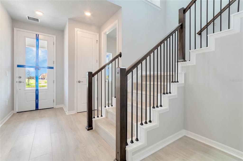 A bright entryway features light wood flooring, a white front door, and a carpeted staircase — 3050 VOYAGER AVENUE, ST CLOUD, FL