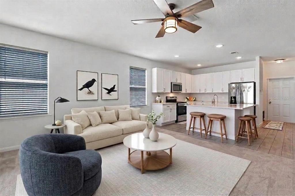 An open-concept living room and kitchen featuring white cabinetry, a sofa, and a circular table — 16021 CHAMPLAIN STREET, CLERMONT, FL