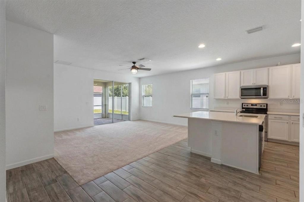 An open-concept living room with carpeted flooring flows into a kitchen with white cabinets — 16021 CHAMPLAIN STREET, CLERMONT, FL