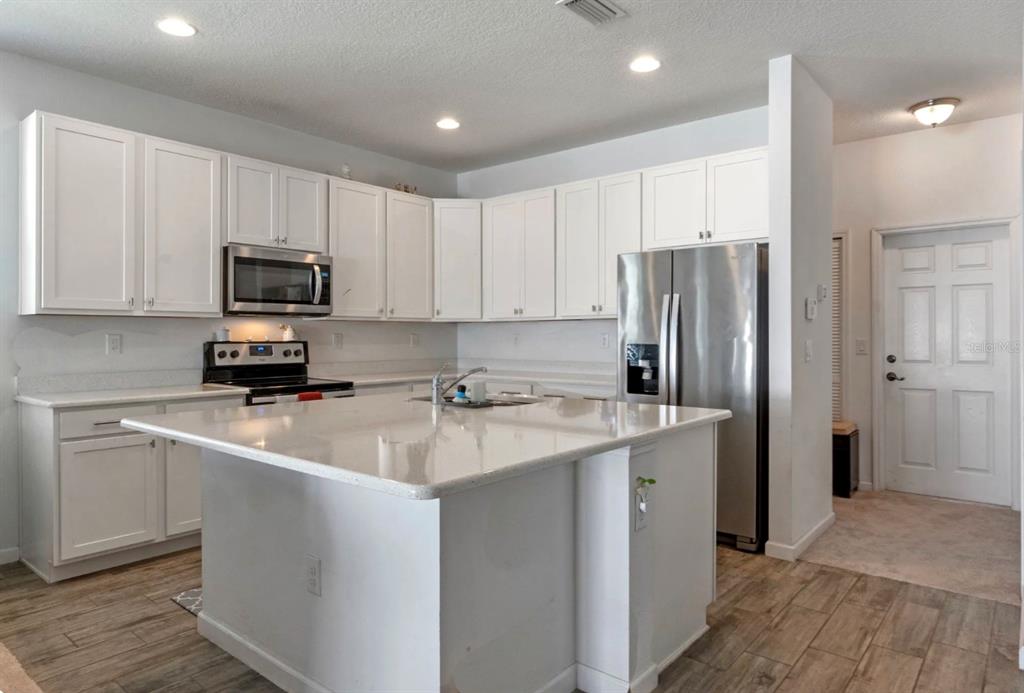 An open-concept kitchen with white cabinets and an island overlooks a carpeted living area — 16021 CHAMPLAIN STREET, CLERMONT, FL