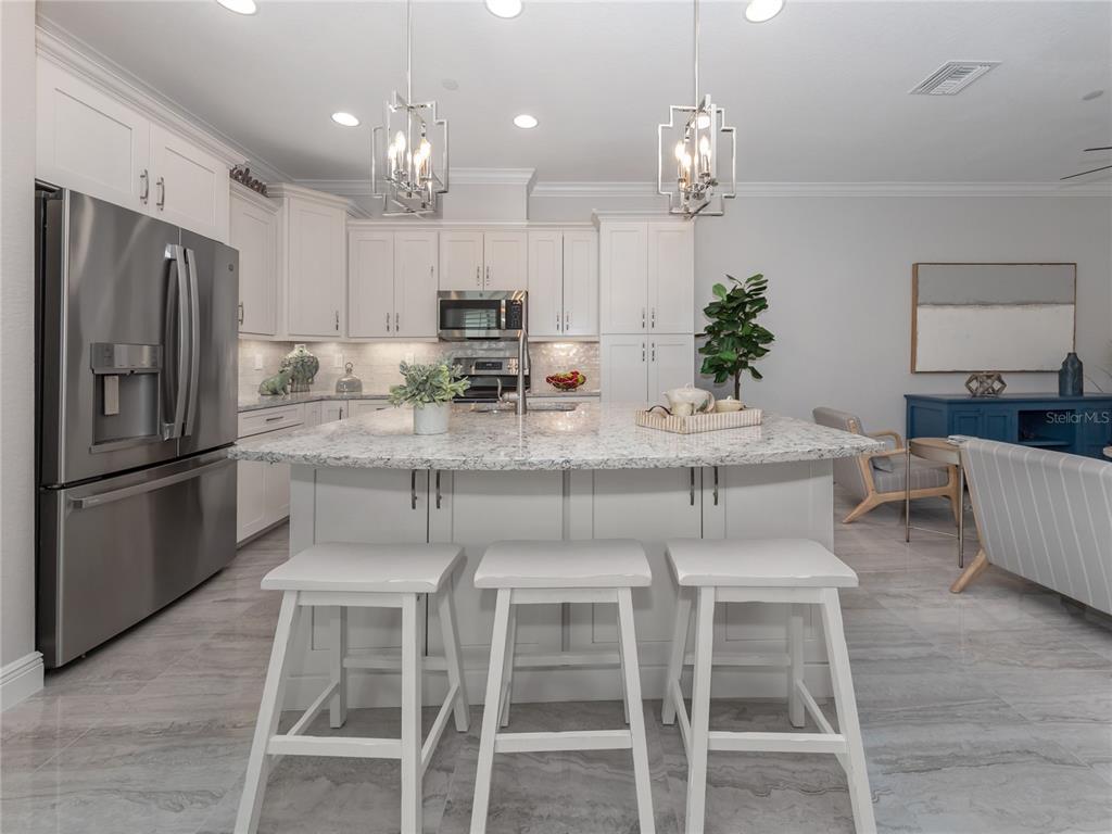 A modern kitchen features white cabinetry, a granite-topped island, stainless steel appliances, and tile flooring — 934 E VENICE AVENUE, VENICE, FL