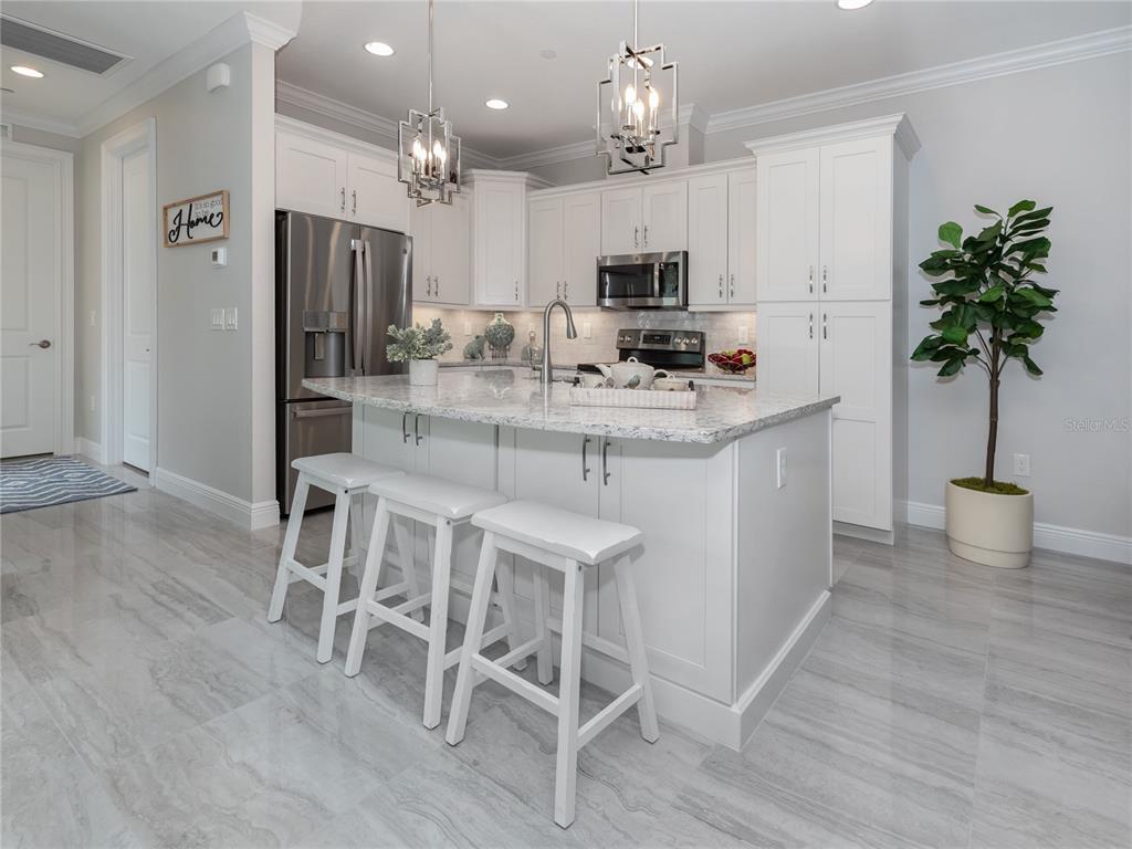 A modern kitchen features white cabinetry, a granite-topped island with three stools, and stainless appliances — 934 E VENICE AVENUE, VENICE, FL