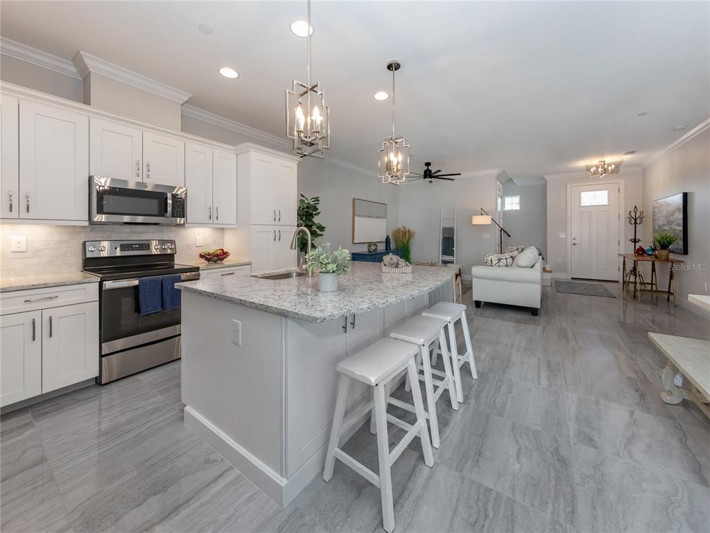 A modern kitchen features white cabinetry, a granite-topped island with stools, and gray tile flooring — 934 E VENICE AVENUE, VENICE, FL