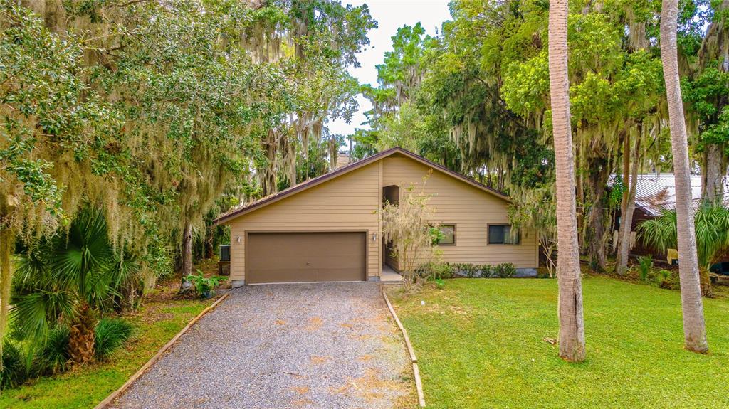 A tan, single-story house with a gravel driveway and a two-car garage under Spanish moss — 121 N LAKE GEORGE DRIVE, GEORGETOWN, FL