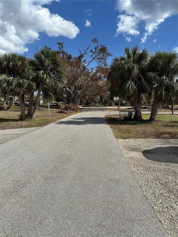 A paved driveway leads toward a residential street lined with palm trees and large trees — 120 SPANIARDS ROAD, PLACIDA, FL