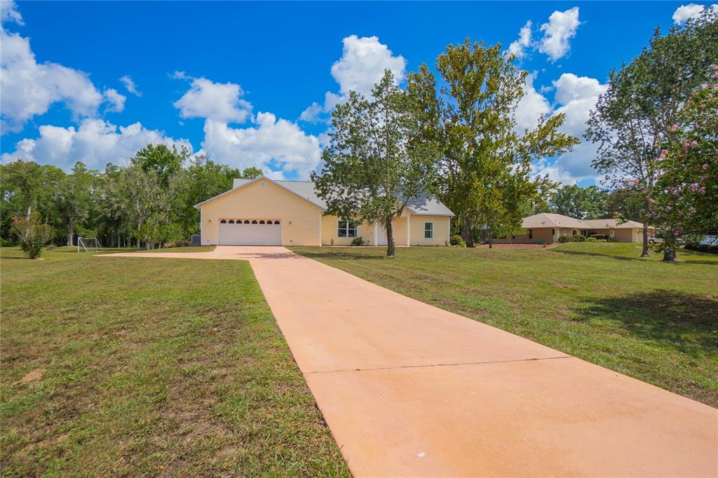 A yellow single-story house with a long concrete driveway and a two-car garage — 12718 SUGAR CREEK BOULEVARD, HUDSON, FL