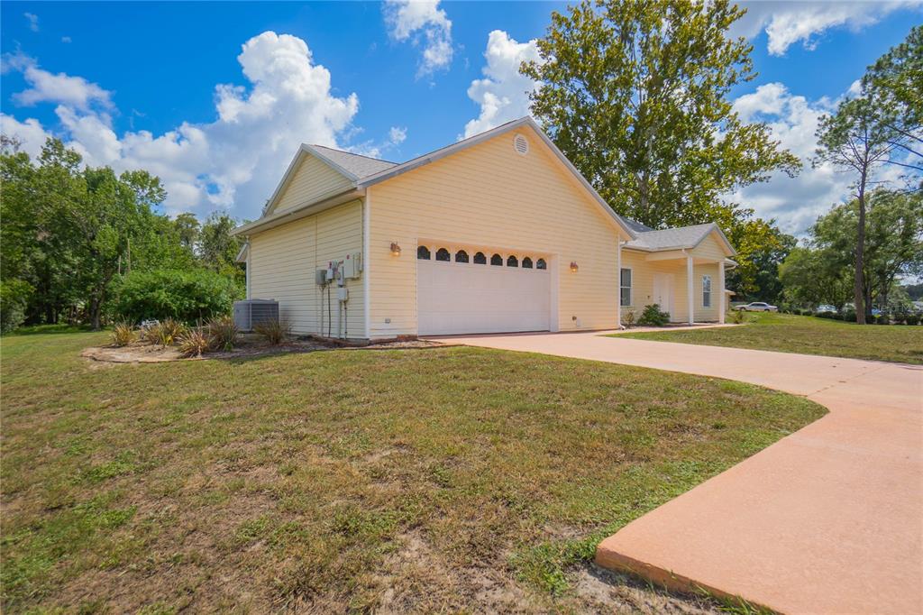 A light yellow house with a two-car garage and a concrete driveway under a blue sky — 12718 SUGAR CREEK BOULEVARD, HUDSON, FL