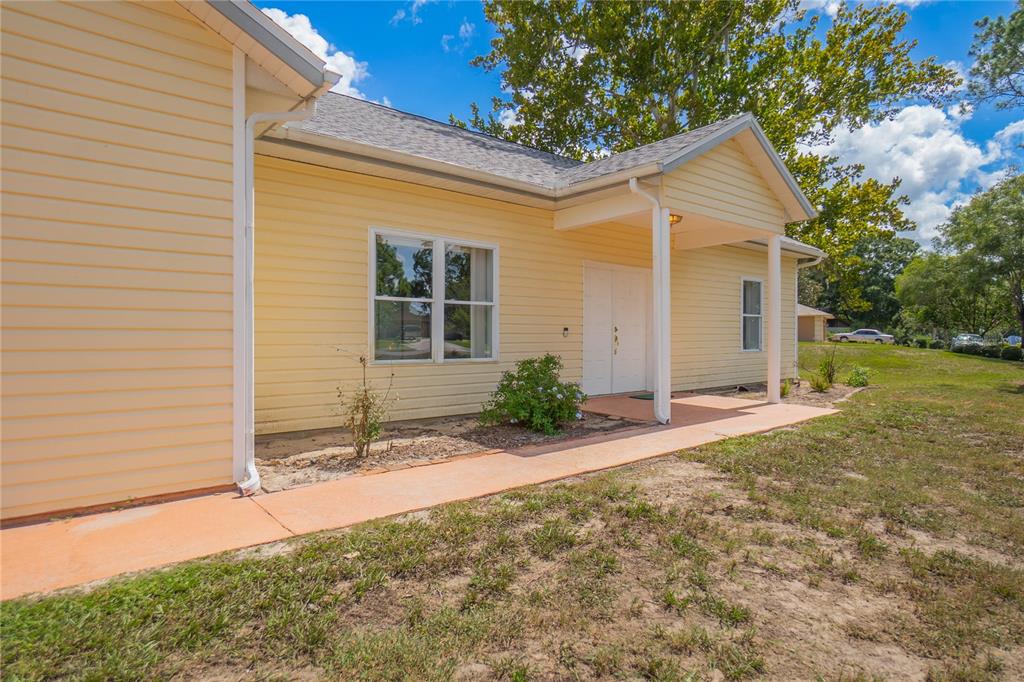 A yellow-sided house with a covered porch, white double doors, and a concrete walkway — 12718 SUGAR CREEK BOULEVARD, HUDSON, FL
