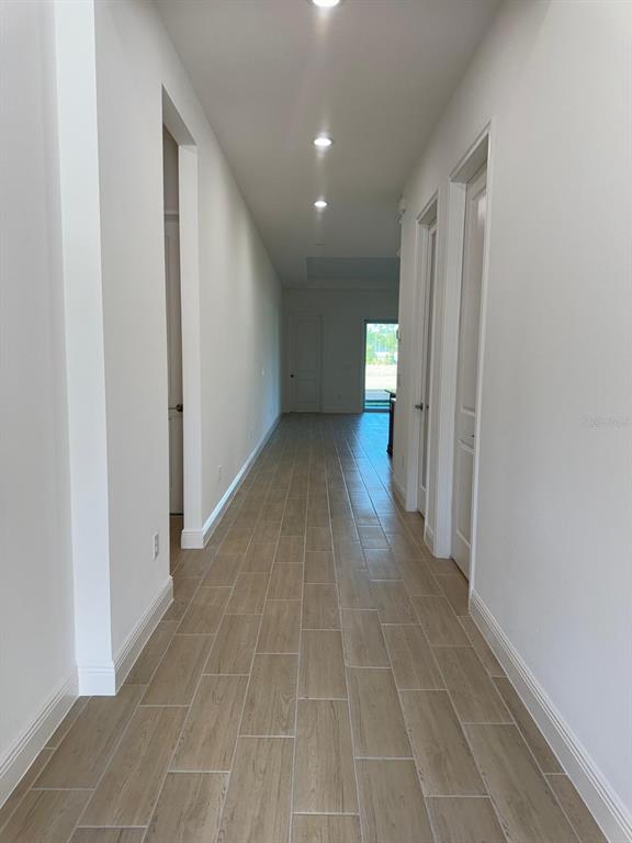 A long hallway with light-colored wood-look tile flooring and white walls leads to a doorway — 1138 CLIFFHAVEN COURT, ORMOND BEACH, FL