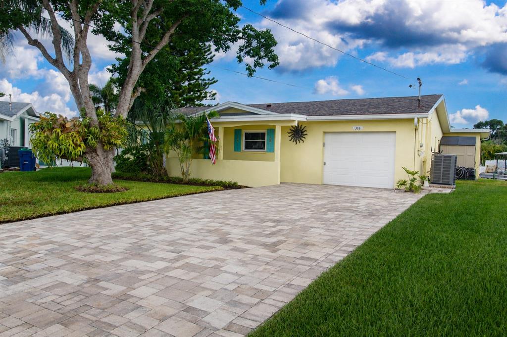 A yellow single-story house features a paved driveway, a white garage door, and a porch — 318 CIRCLE DRIVE, PALM HARBOR, FL