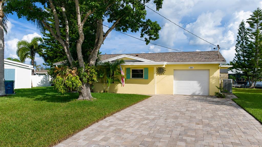 A yellow single-story house with a paved driveway, a garage, and a large front tree — 318 CIRCLE DRIVE, PALM HARBOR, FL