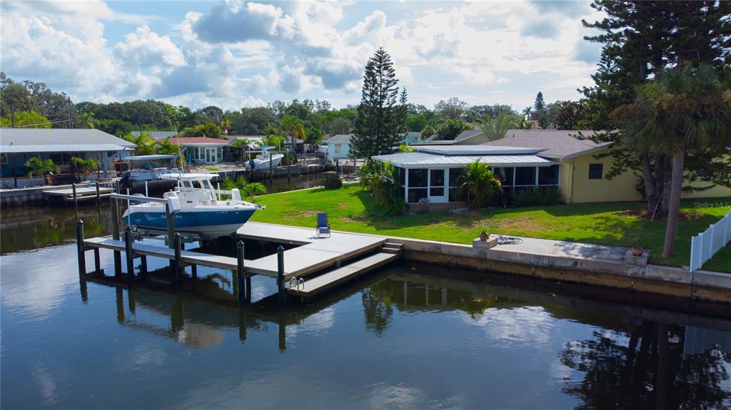 A blue boat sits on a lift at a dock next to a waterfront house — 318 CIRCLE DRIVE, PALM HARBOR, FL