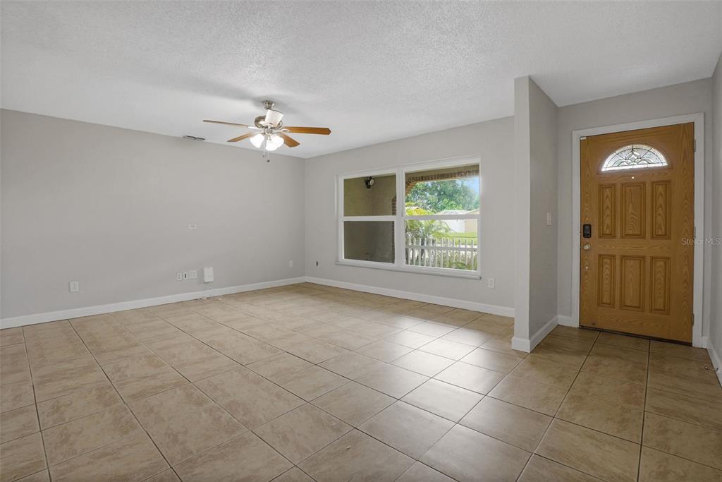 An empty living room features light-colored tile flooring, gray walls, a ceiling fan, and a wooden door — 169 LEISURE CIRCLE, PORT ORANGE, FL