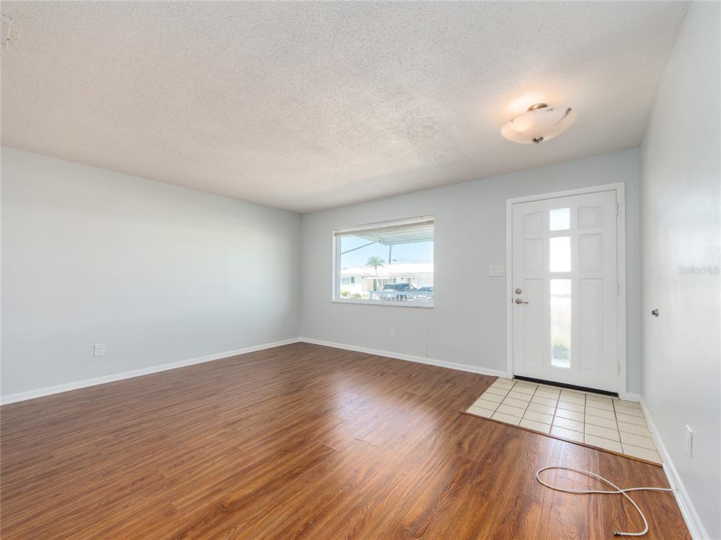 An empty living room features wood-look flooring, light blue walls, and a white front door — 9157 140TH WAY, SEMINOLE, FL