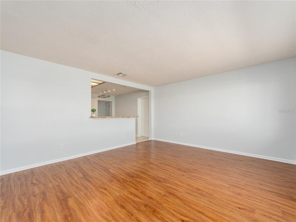 An empty room with light-colored walls, wood-look flooring, and a pass-through window to the kitchen — 9157 140TH WAY, SEMINOLE, FL