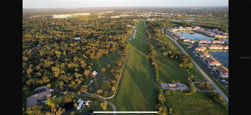 An aerial view shows a long, narrow grassy corridor separating a wooded area from residential buildings — 12200 SW ACADEMY DRIVE, ARCADIA, FL