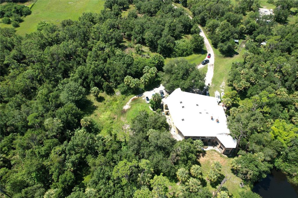 An aerial view shows a large house with a white roof surrounded by dense forest — 12200 SW ACADEMY DRIVE, ARCADIA, FL
