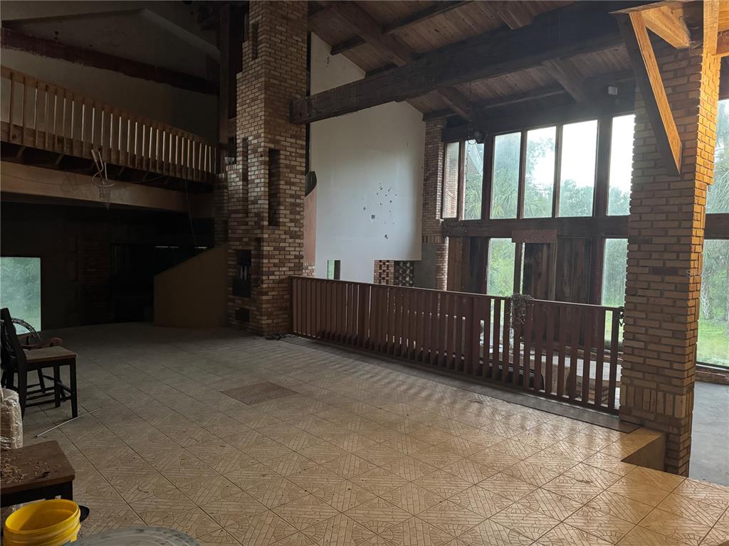 A spacious room features a brick fireplace, wooden ceiling beams, and a balcony overlooking windows — 12200 SW ACADEMY DRIVE, ARCADIA, FL