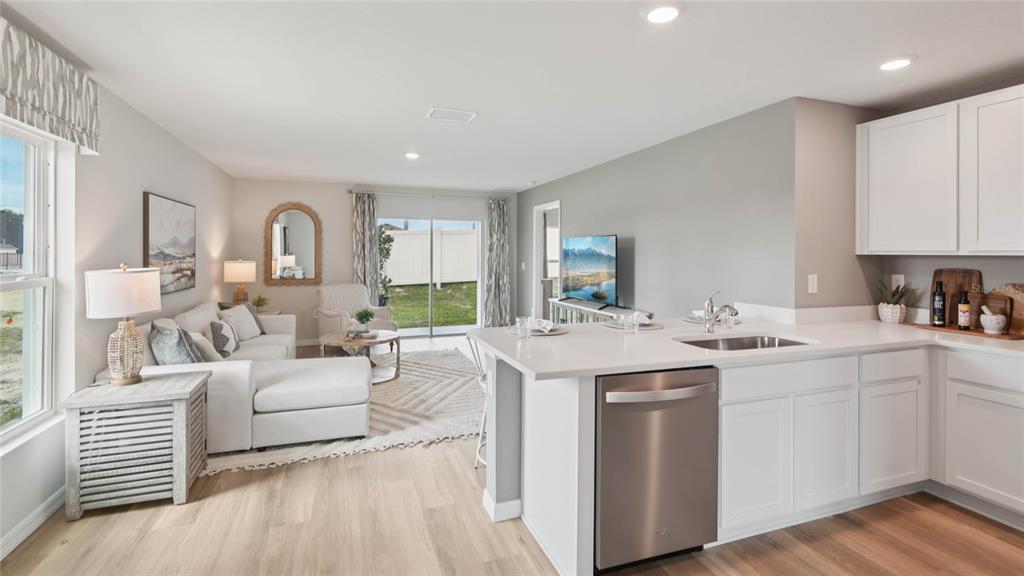 A bright open-concept kitchen and living area with white cabinetry, stainless appliances, and light flooring — 24324 NW 10TH ROAD, NEWBERRY, FL