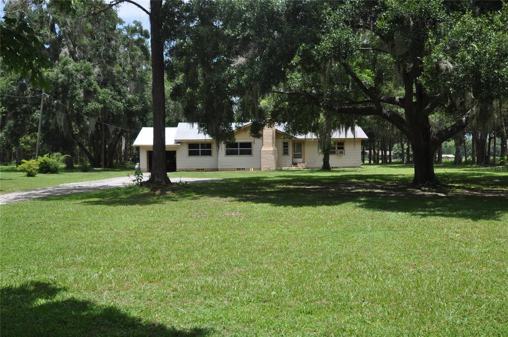 A single-story house with a metal roof and a large yard surrounded by mature trees — 18491 NE STATE ROAD 121, WILLISTON, FL
