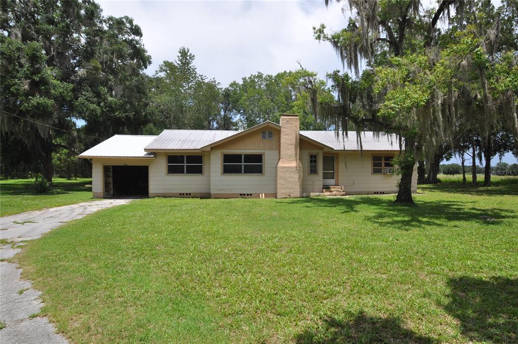 A single-story house with a metal roof, brick chimney, and attached garage sits on grass — 18491 NE STATE ROAD 121, WILLISTON, FL