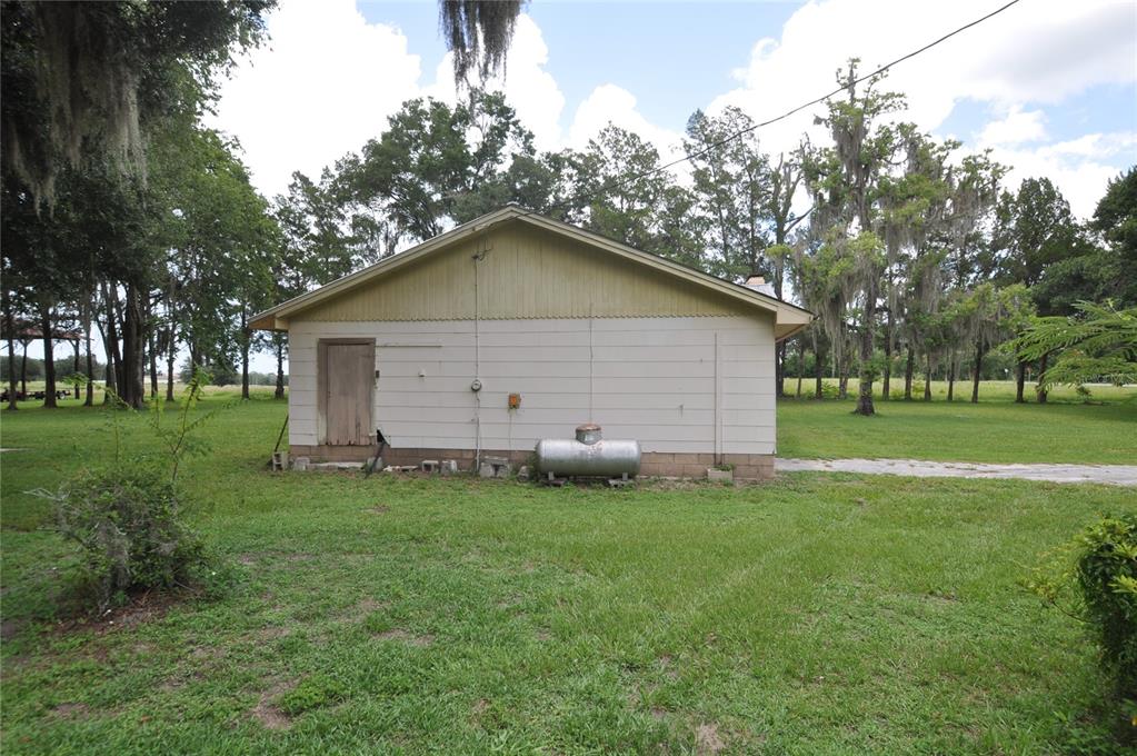 The exterior side of a single-story house features light-colored siding, a door, and a propane tank — 18491 NE STATE ROAD 121, WILLISTON, FL