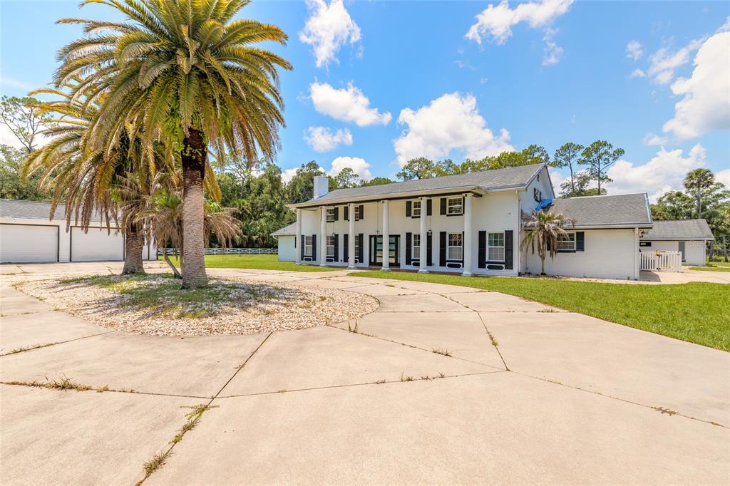 A two-story white house with a columned porch stands behind a large concrete driveway — 2015 HALIFAX DRIVE, PORT ORANGE, FL