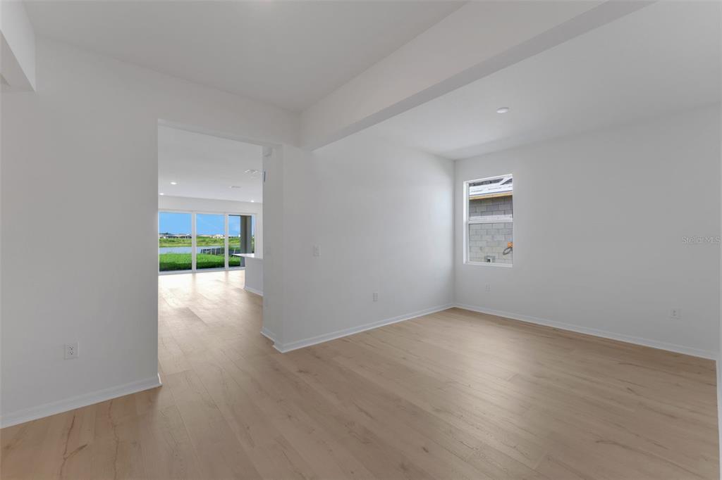 An empty room with light wood-look flooring leads to an open living area with water views — 16938 SQUIRREL BRANCH LANE, ALVA, FL