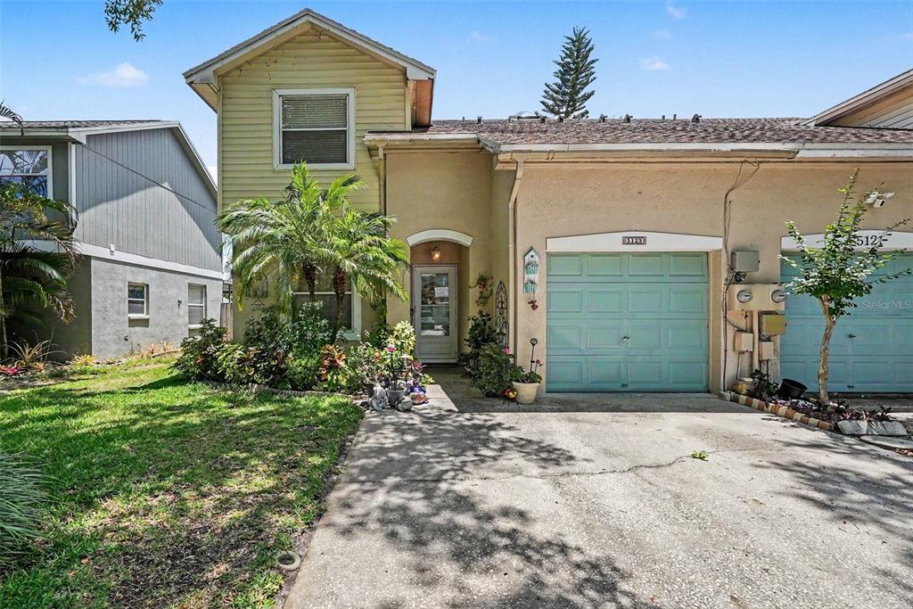 A two-story townhouse with yellow siding, a light-colored stucco facade, and a teal garage door — 5123 CORVETTE DRIVE, TAMPA, FL