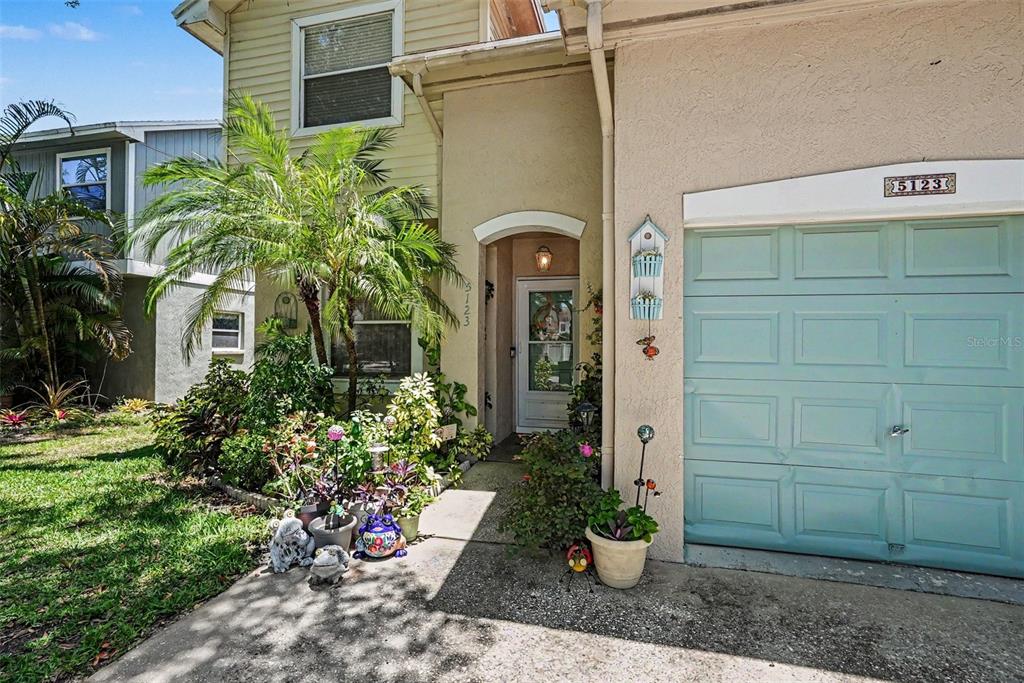A light-colored house exterior features a blue garage door, a front entrance, and potted plants — 5123 CORVETTE DRIVE, TAMPA, FL