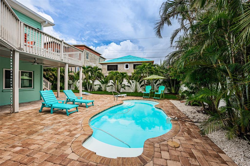 A backyard features a swimming pool, brick patio, two lounge chairs, and a two-story house — 16109 3RD STREET E, REDINGTON BEACH, FL
