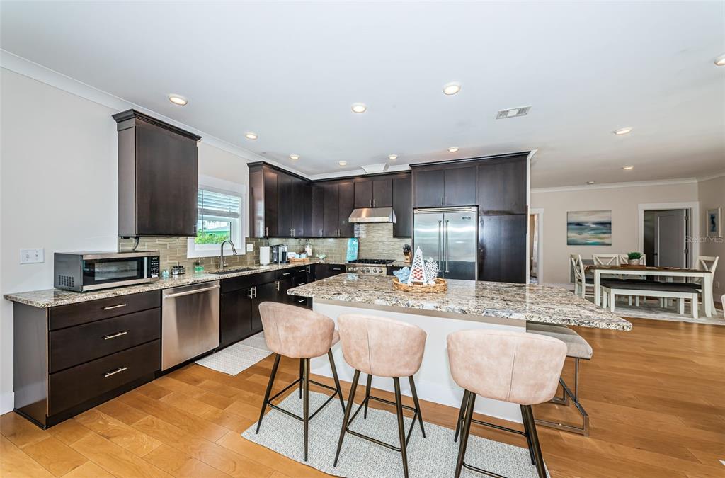 A kitchen features dark wood cabinets, granite countertops, a central island, and three bar stools — 16109 3RD STREET E, REDINGTON BEACH, FL