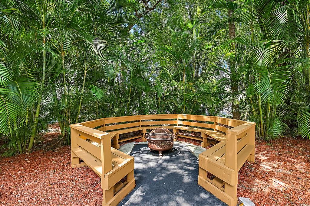 A wooden bench surrounds a fire pit in a backyard area with lush palm trees — 507 LAKESHORE DRIVE, EUSTIS, FL