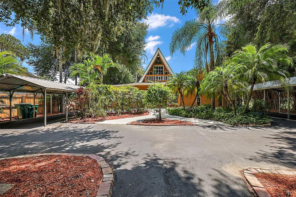 A house with an A-frame roof and two carports sits behind a paved driveway — 507 LAKESHORE DRIVE, EUSTIS, FL