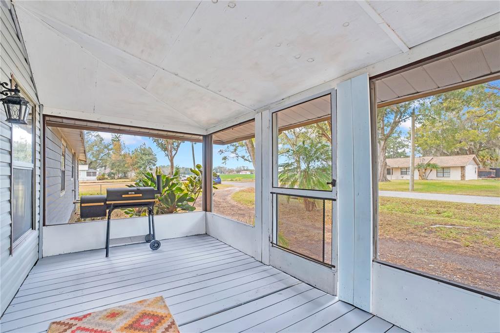 A screened-in porch with gray wooden flooring, a charcoal grill, and a screen door — 13713 WALDEN SHEFFIELD ROAD, DOVER, FL
