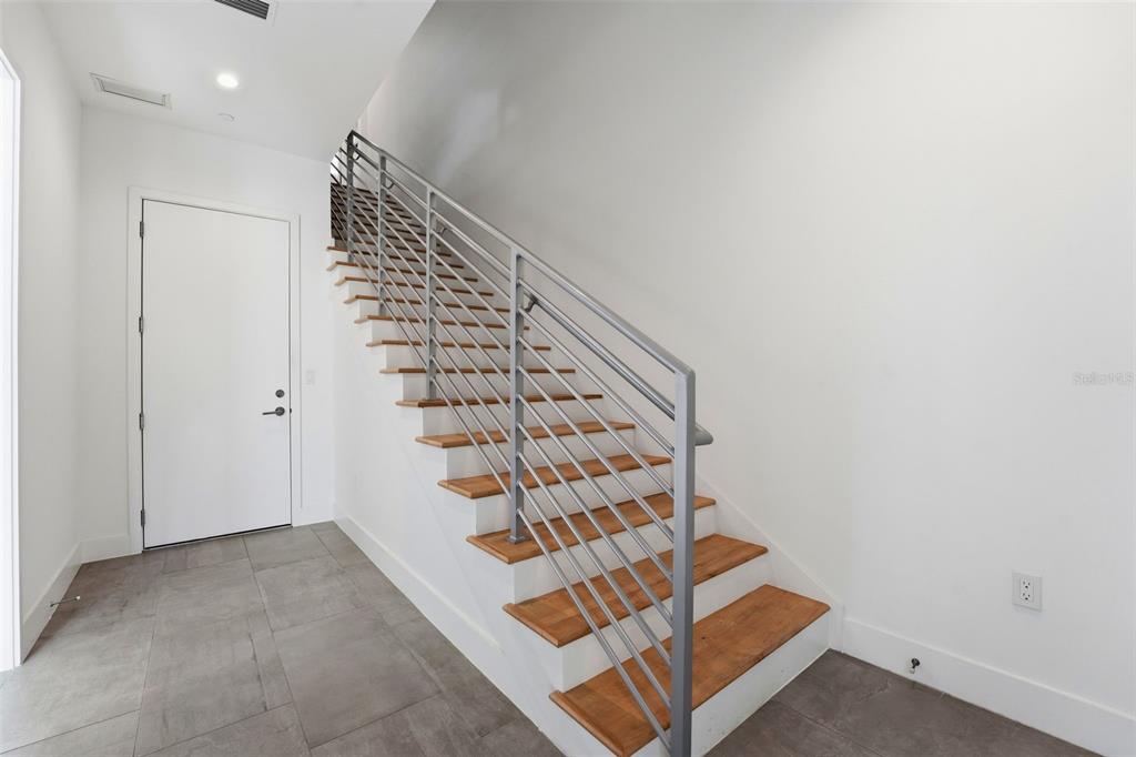 A staircase with wooden treads and a metal railing sits beside a white door — 620 RAWLS AVENUE, SARASOTA, FL