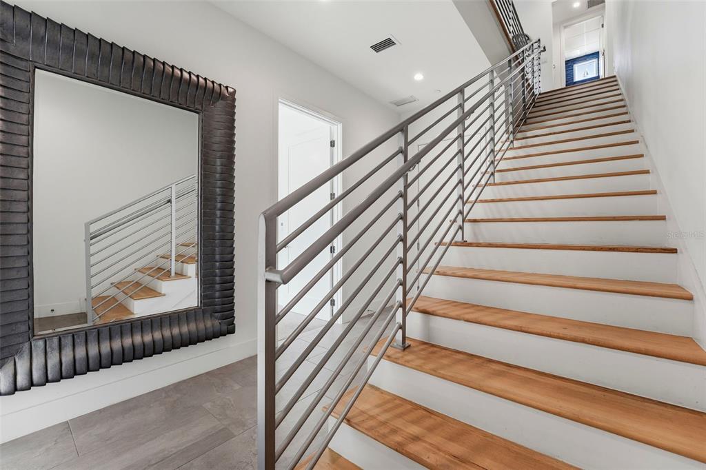 A staircase with wooden treads and a metal railing sits beside a large decorative mirror — 620 RAWLS AVENUE, SARASOTA, FL