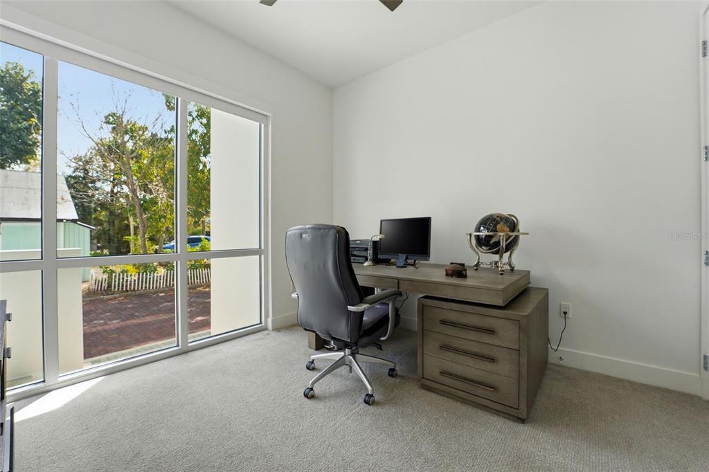 A home office with a desk, chair, and large windows overlooking a residential street — 620 RAWLS AVENUE, SARASOTA, FL